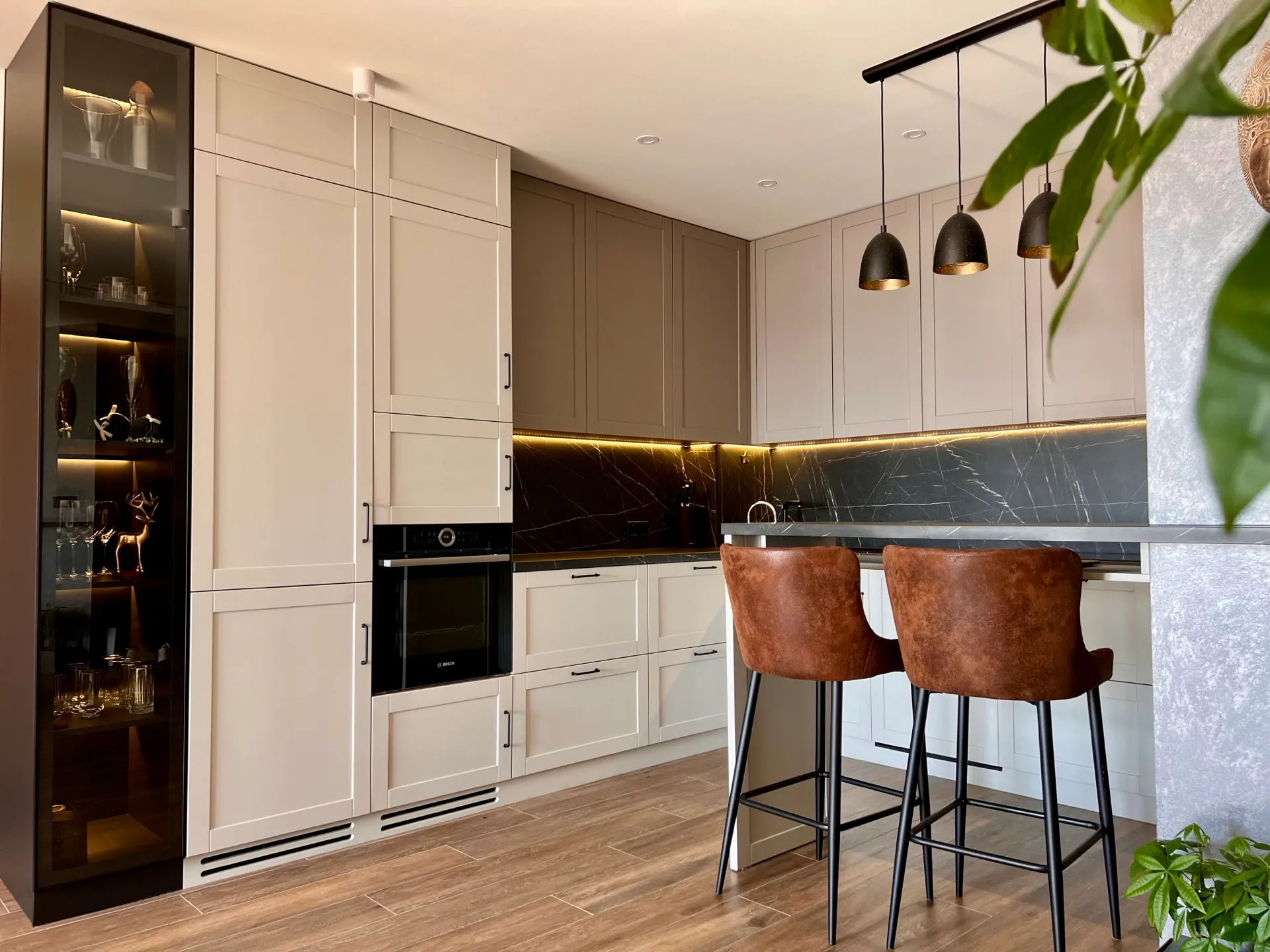 Modern kitchen with beige cabinets, black marble backsplash, bar counter, and brown leather stools under pendant lights.