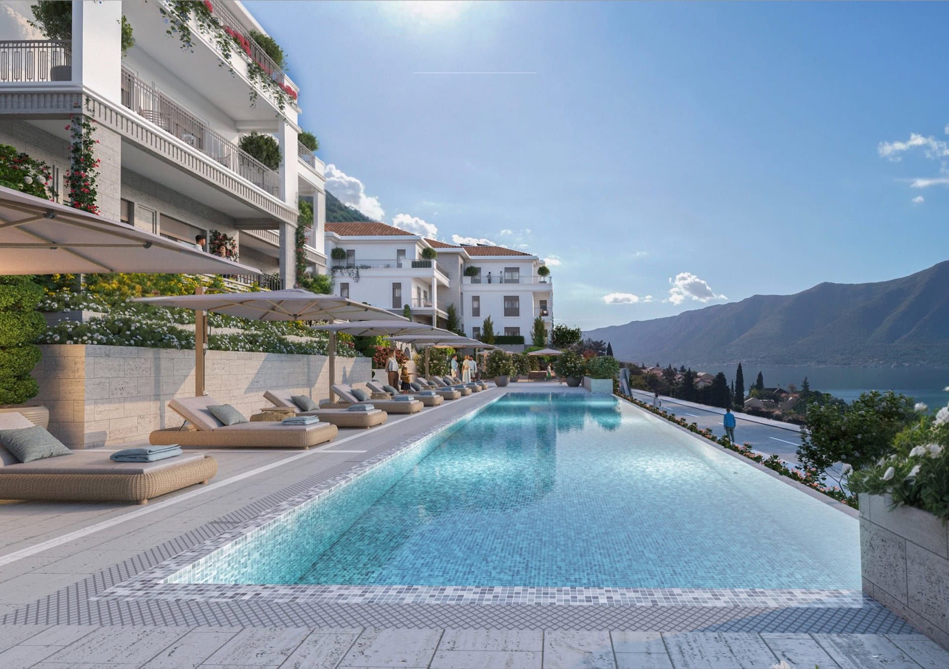 An outdoor pool with sun loungers in a luxury residential complex in Ljuta, Montenegro, with views of the mountains and the Adriatic Sea.