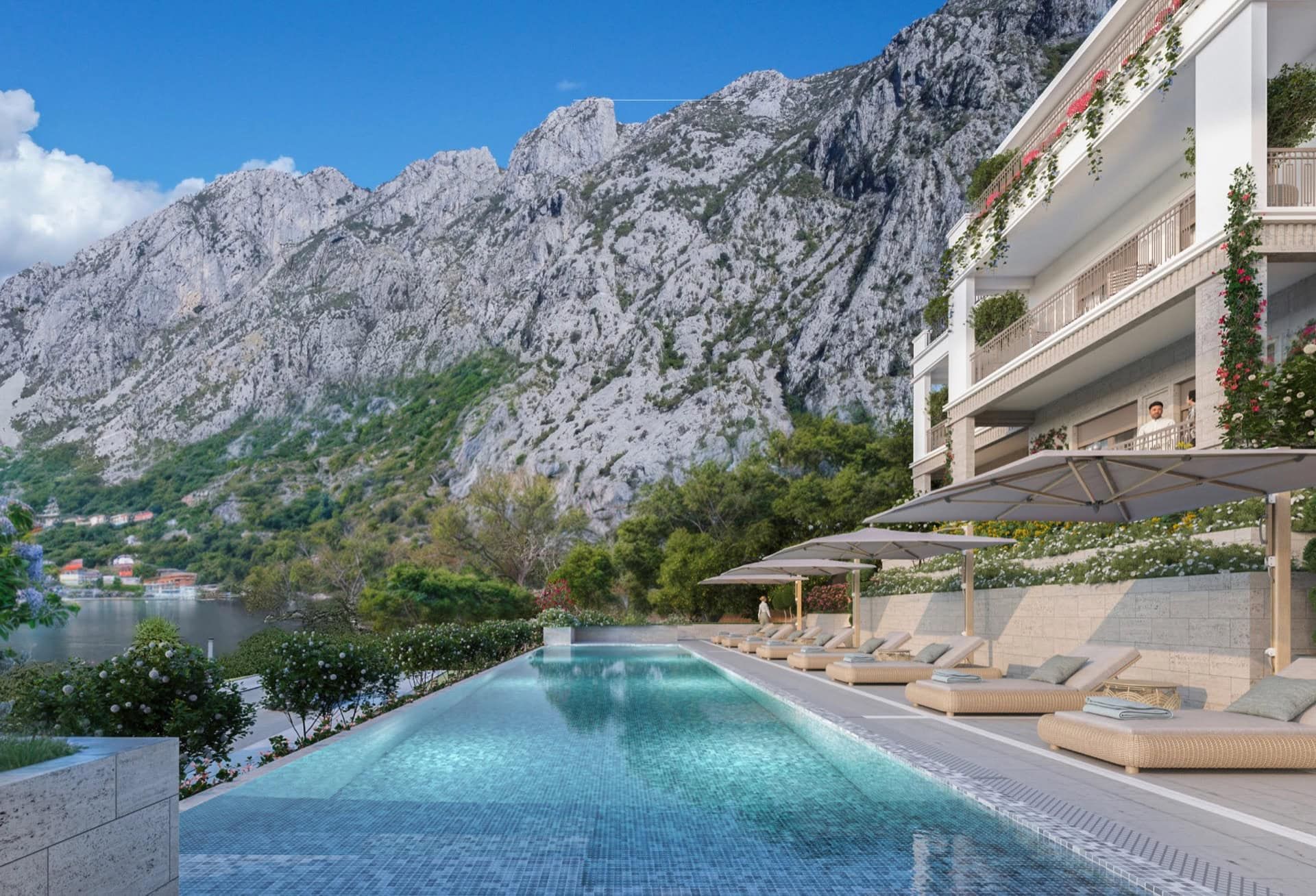 Swimming pool with sun loungers in a residential complex in Ljuta, Montenegro, with mountains and the sea coast in the background.