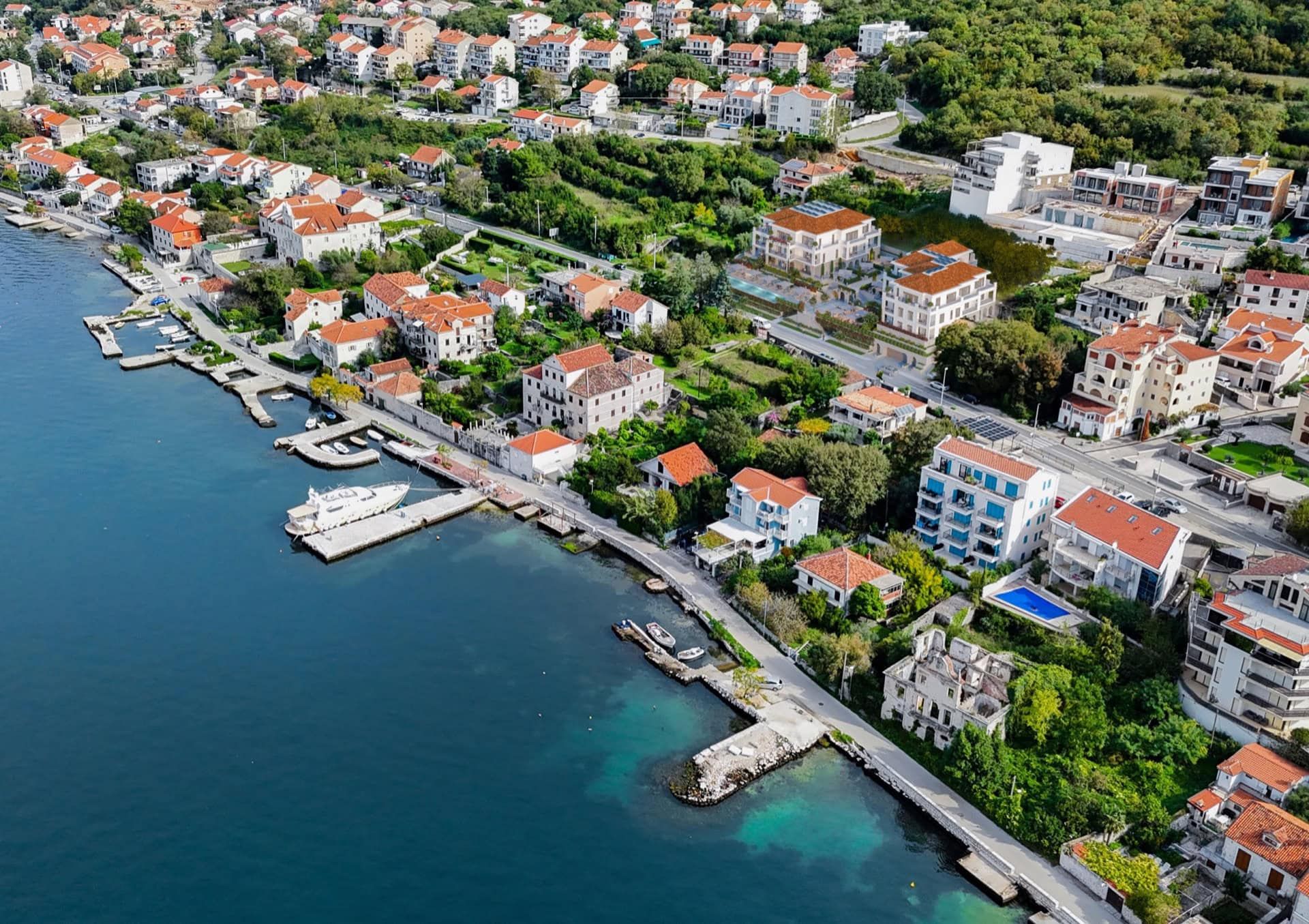 Aerial view of a residential complex in Luštica, Montenegro: coastal houses with red roofs and private piers by the sea.