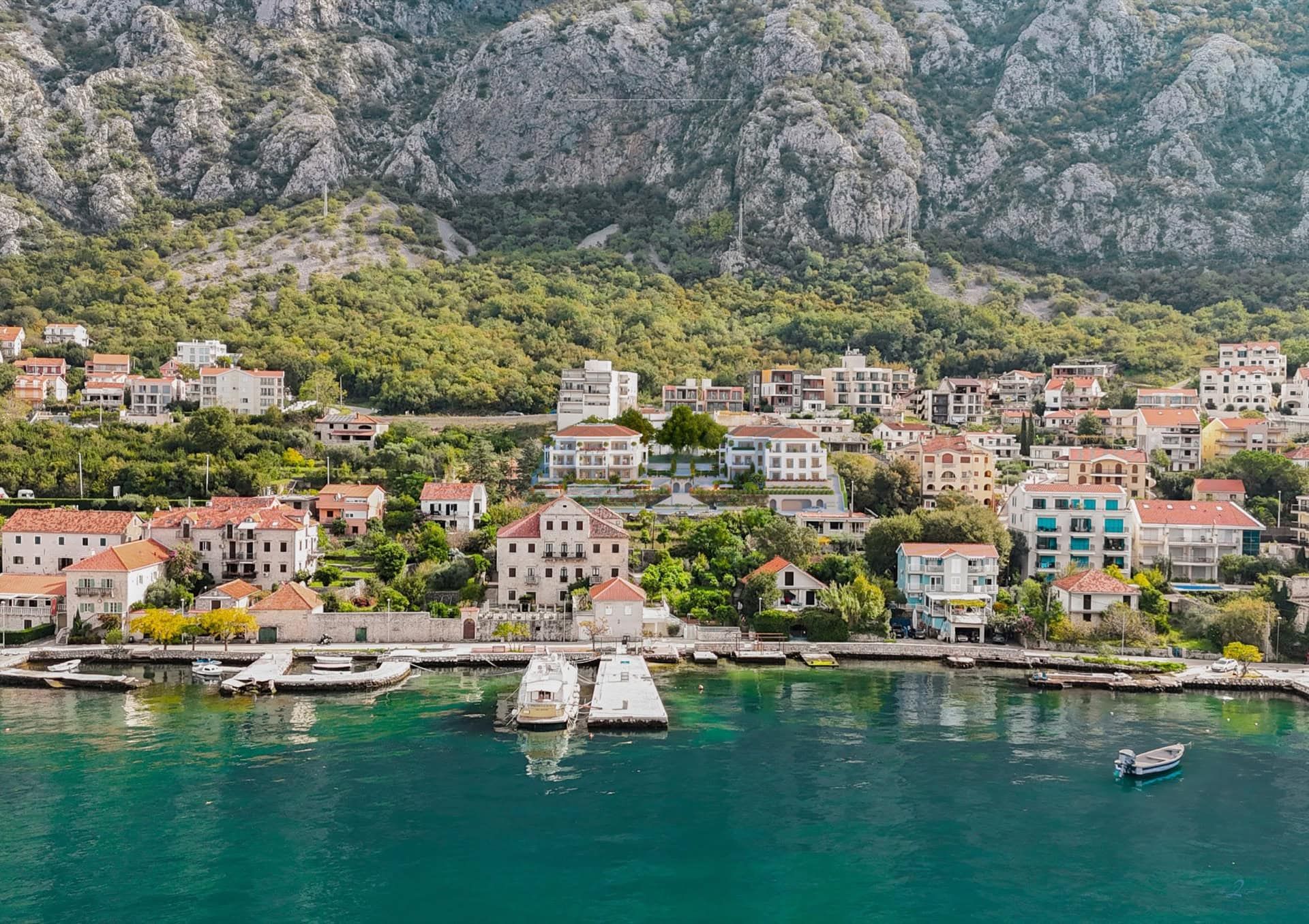 Sea view of a residential complex in Ljuta, Montenegro: coastal houses with tiled roofs, mountains, and a private pier.