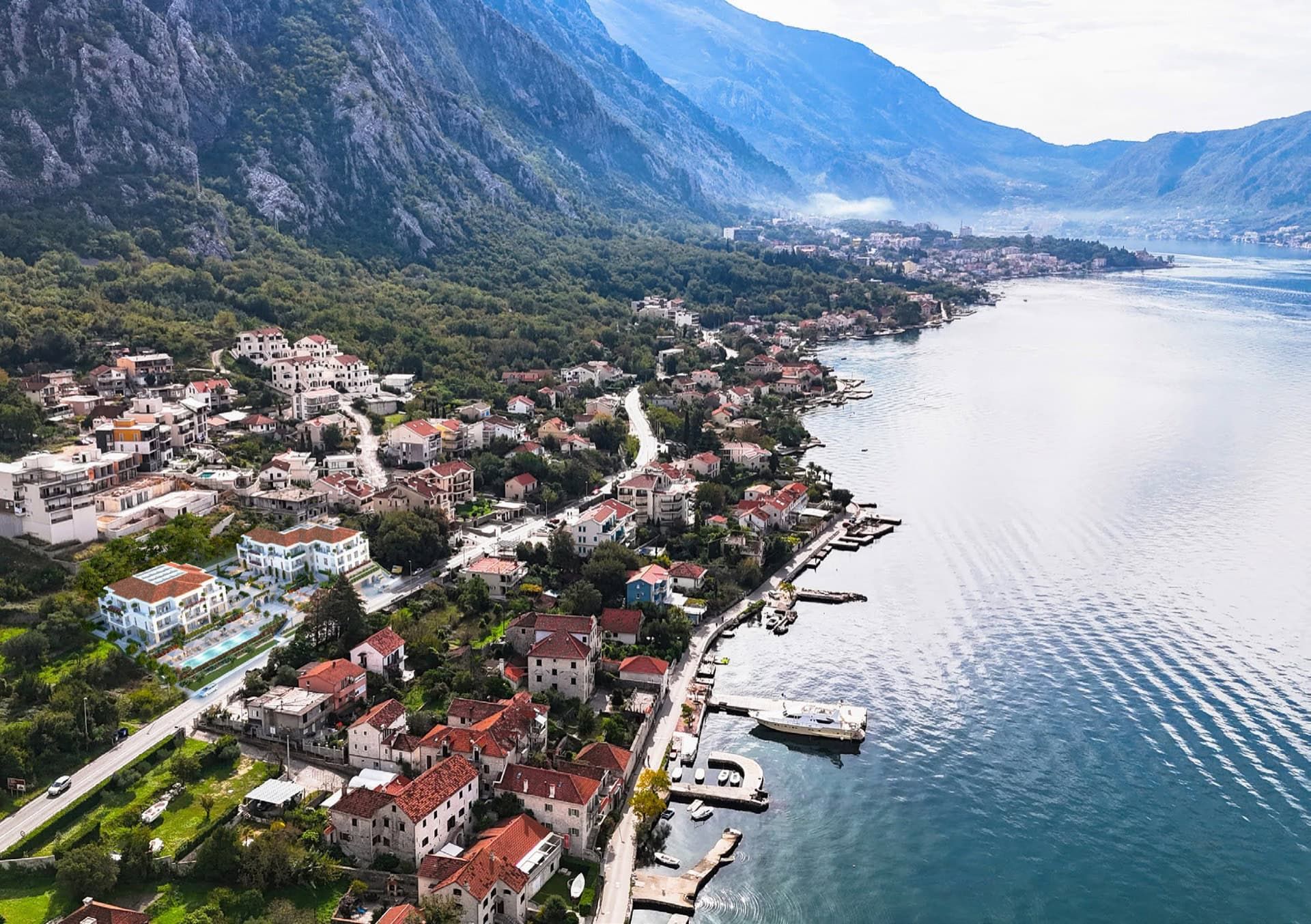 Panoramic view of a residential complex in Ljuta, Montenegro: modern buildings by the sea with a pool and mountain scenery.