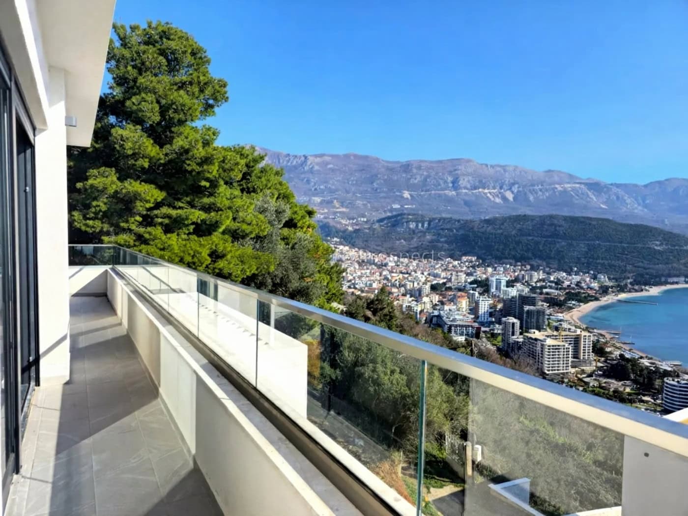 Panoramic view of the sea and Budva from the spacious balcony of a modern villa in Montenegro with a glass railing.