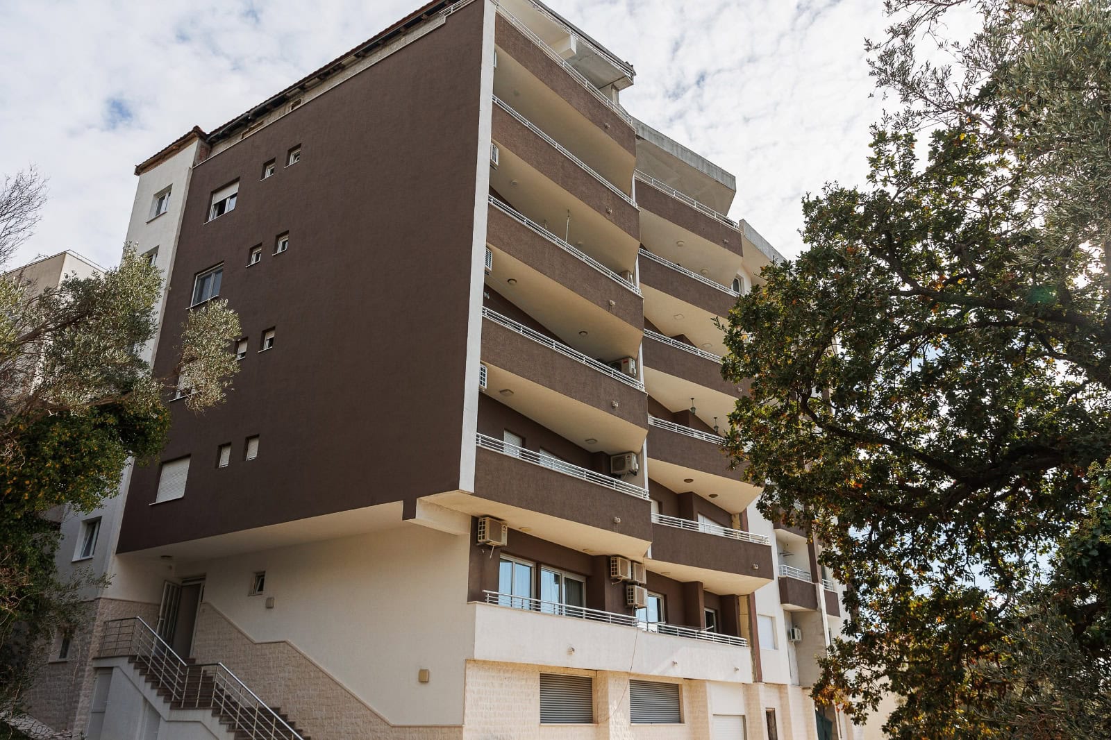 Modern apartment building with balconies in Bečići, Montenegro, front view of the building with trees.