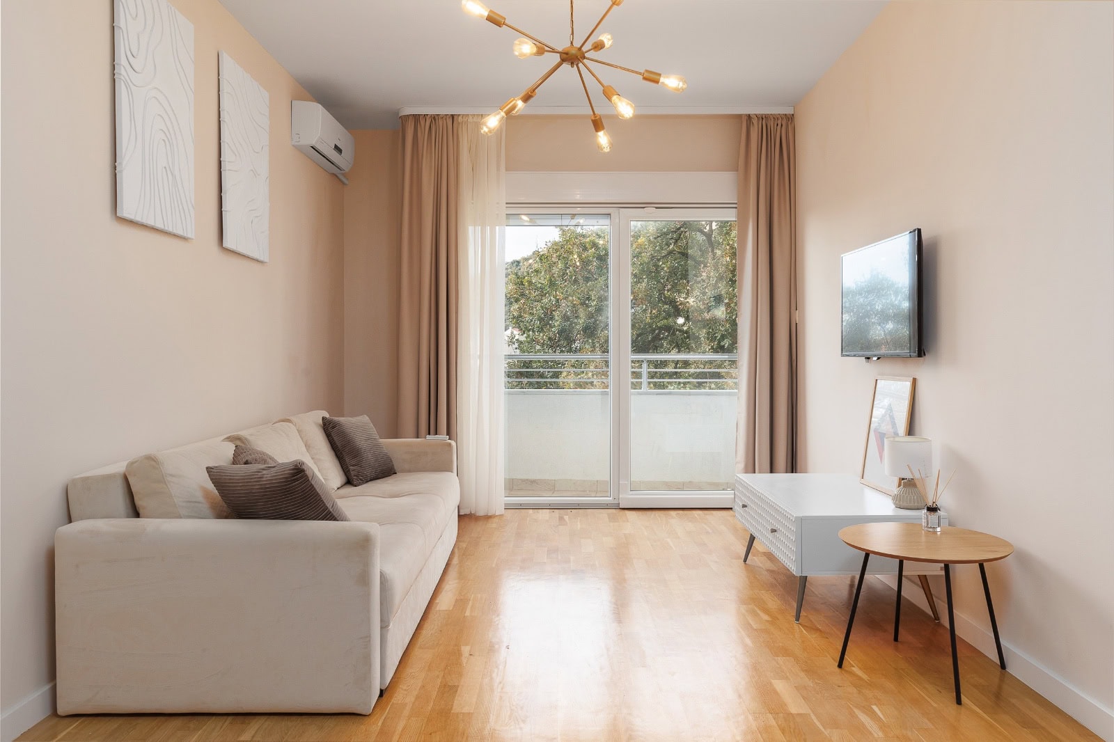 Cozy living room with a beige sofa and access to the balcony in an apartment, Becici, Montenegro. Modern interior with a TV.