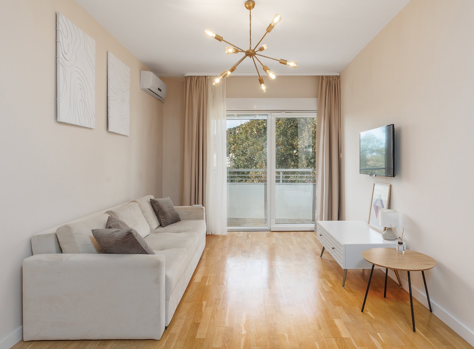 Bright living room in an apartment in Bečići, Montenegro: beige sofa, designer chandelier, access to a balcony with a view.