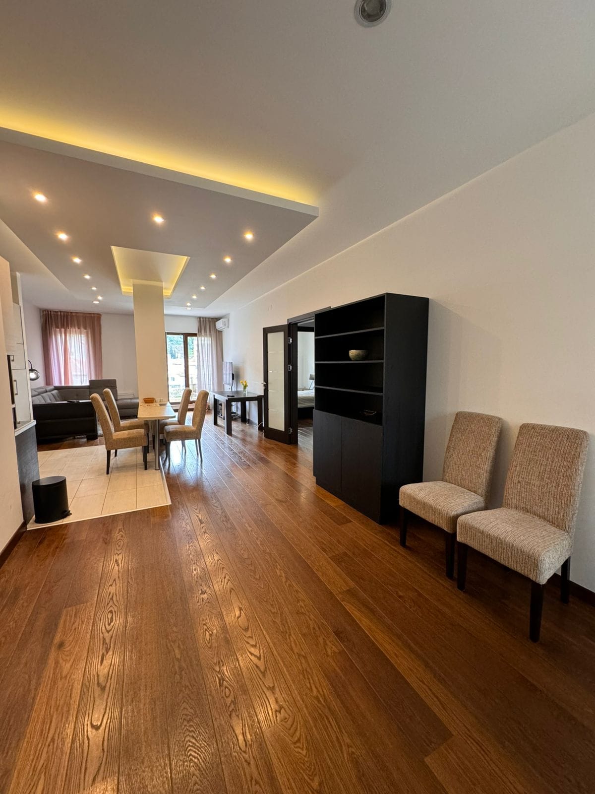 Spacious living room in an apartment in Budva, Montenegro: wooden floor, modern lighting, and dining area.