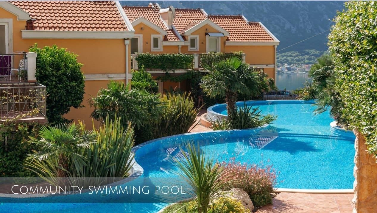 Outdoor pool at a residential complex in Orahovac, Montenegro, with sea and mountain views surrounded by palm trees.
