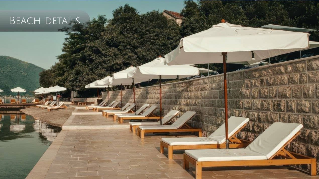 Private beach with sun loungers and umbrellas by a stone wall in Orahovac, Montenegro: seaside relaxation area.