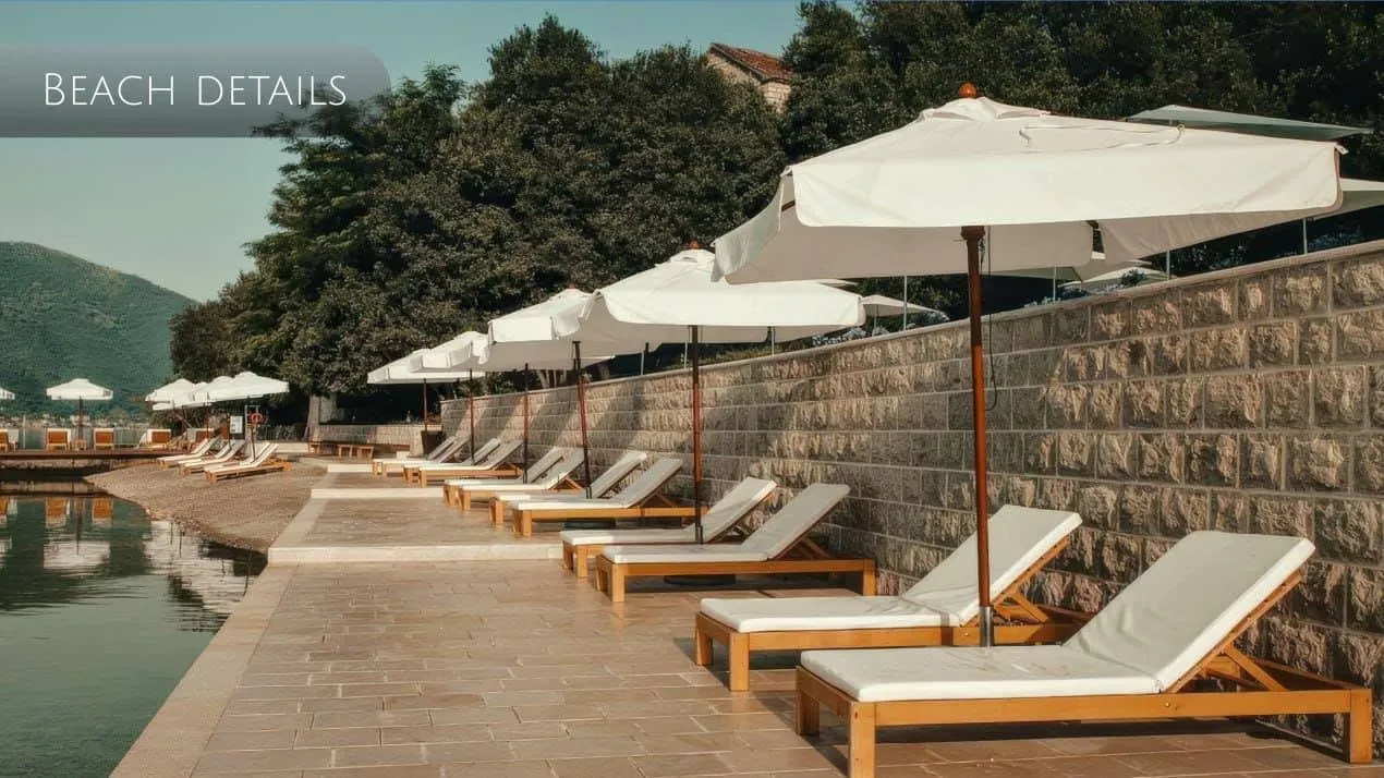Beach area with wooden sunbeds and white umbrellas along a stone wall by the water.