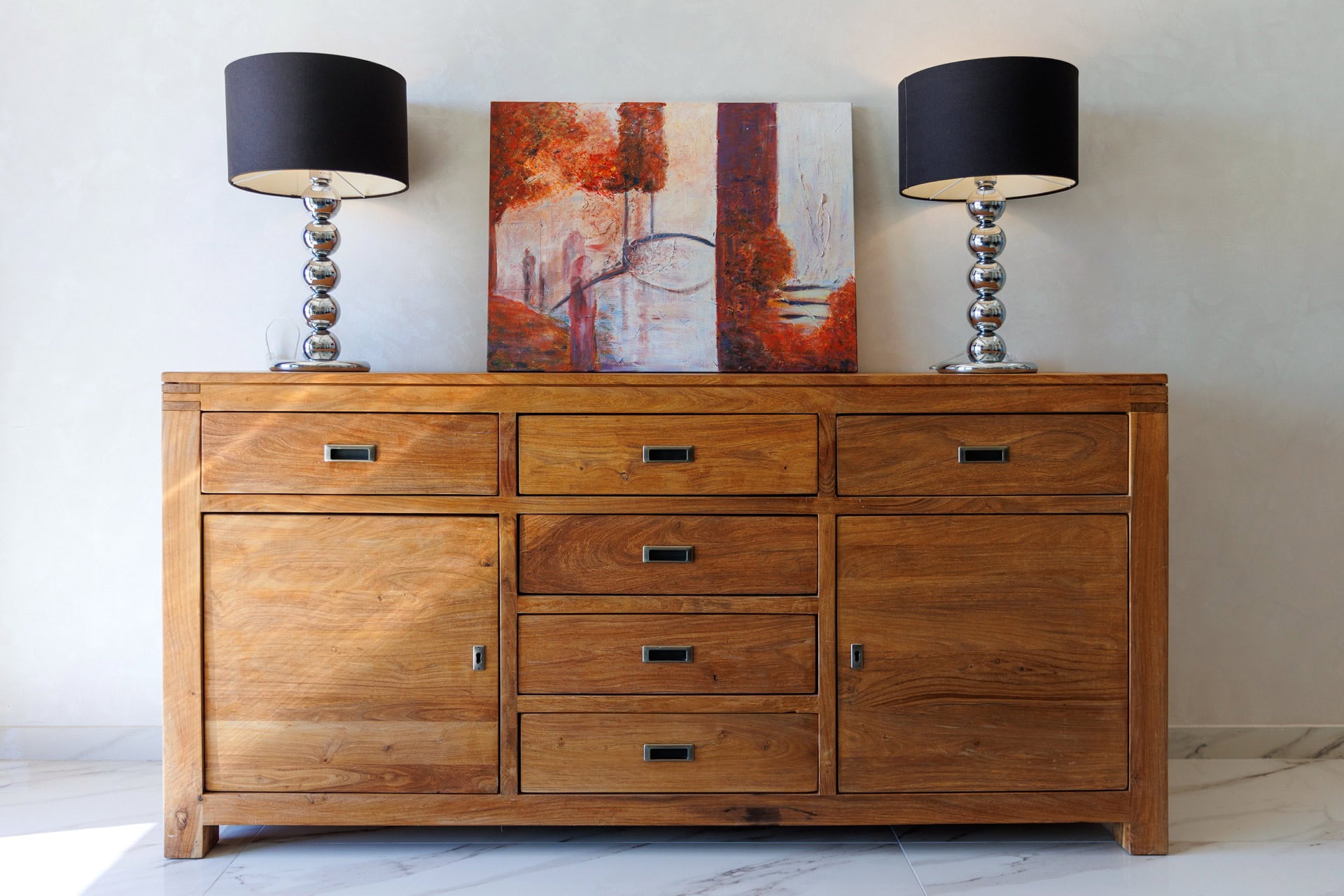 A wooden dresser with a painting and lamps in the living room of an apartment in Bečići, Montenegro.