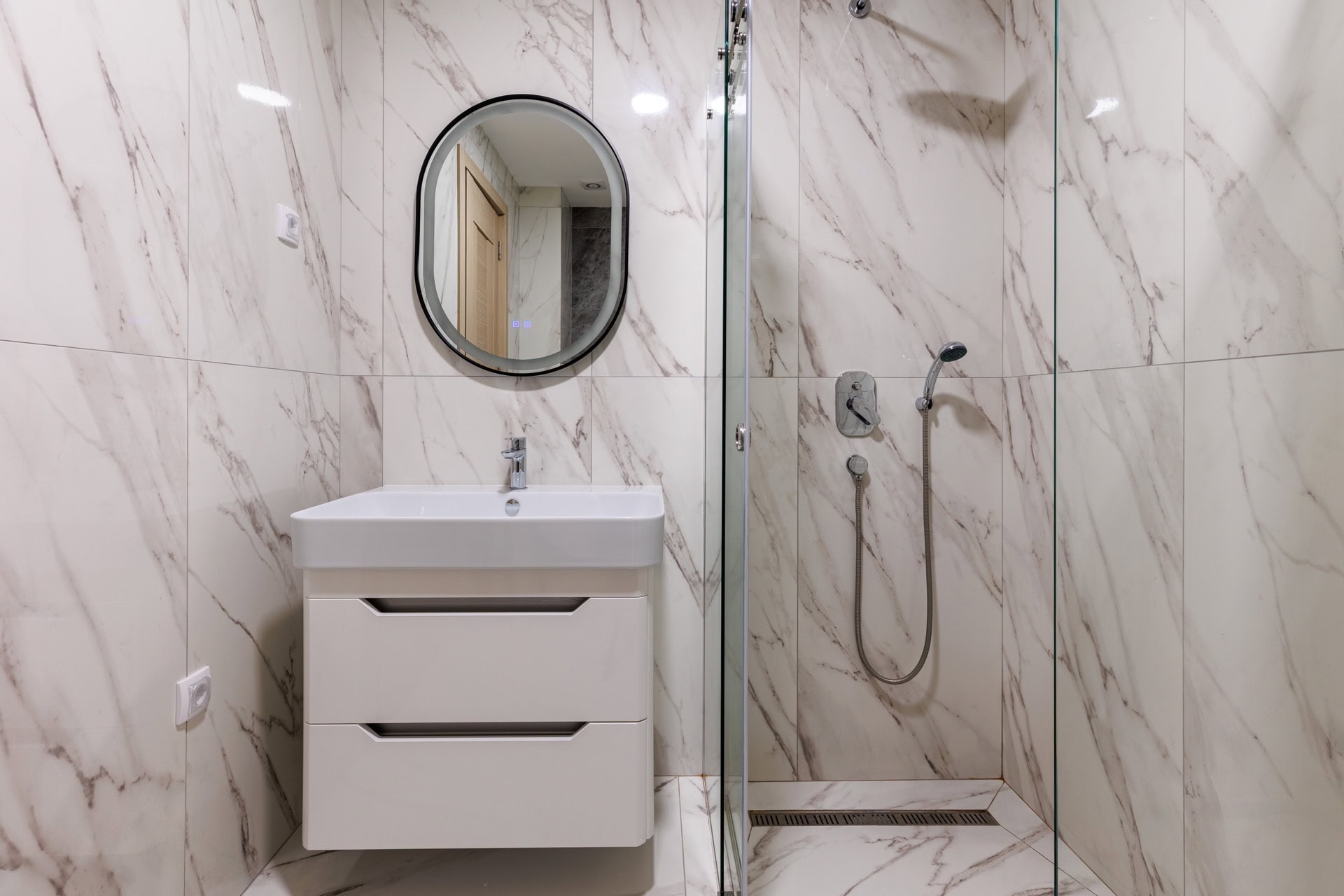 Modern bathroom in an apartment in Bečići, Montenegro: shower cabin, vanity with sink, and illuminated mirror.