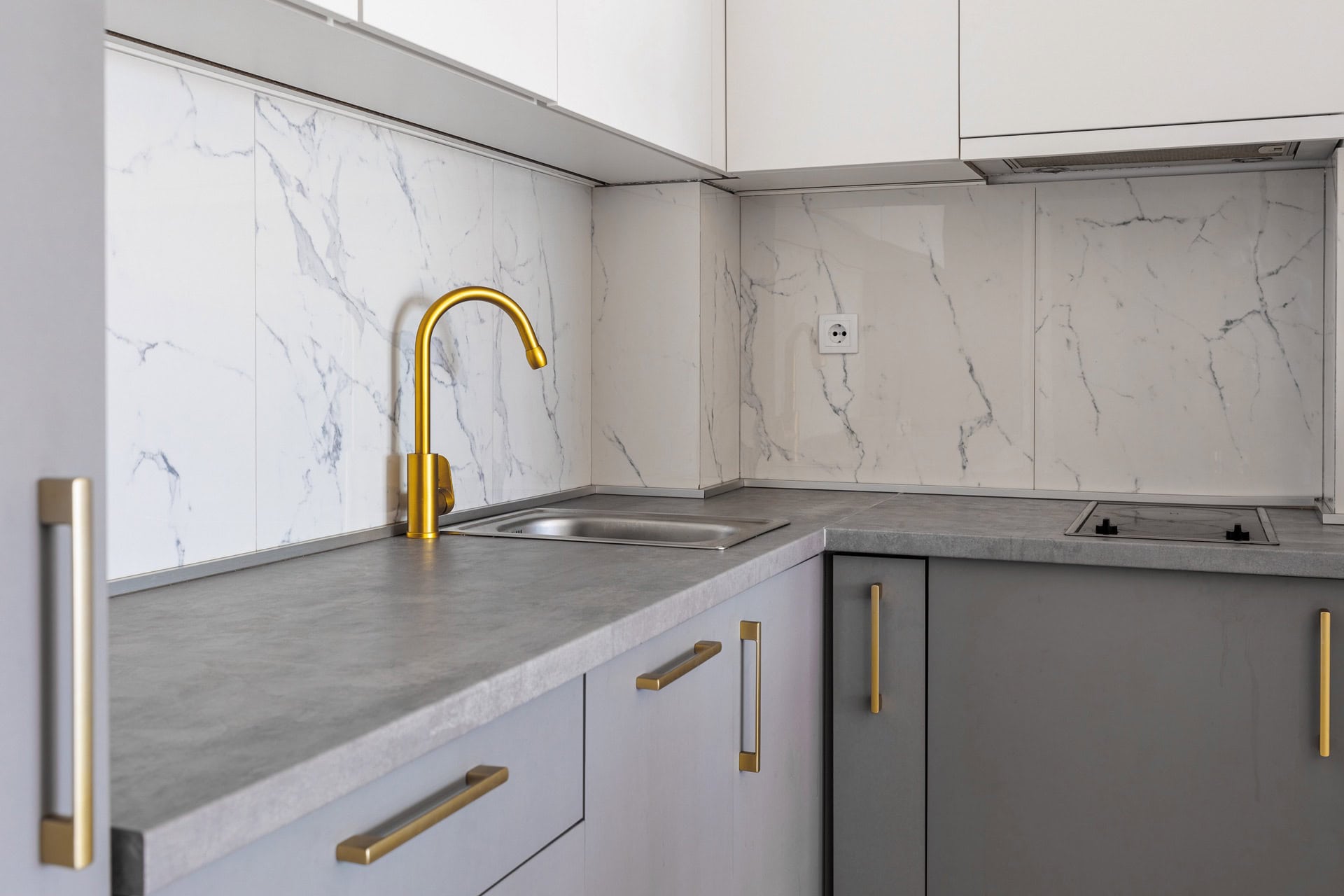 Modern kitchen in an apartment in Bečići, Montenegro: gray cabinets, gold faucet, and a white marble-look backsplash.