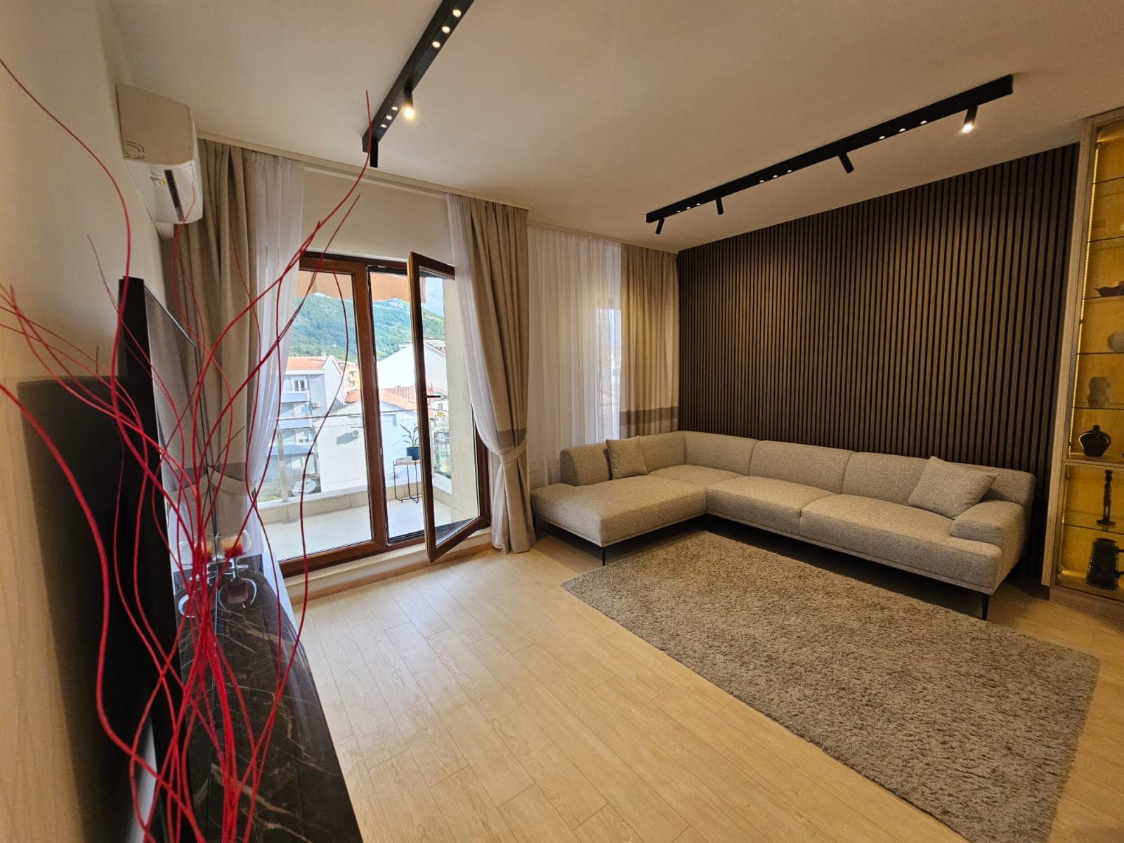 Modern living room in an apartment in Budva, Montenegro: corner sofa, decorative wall slats, and access to the balcony.