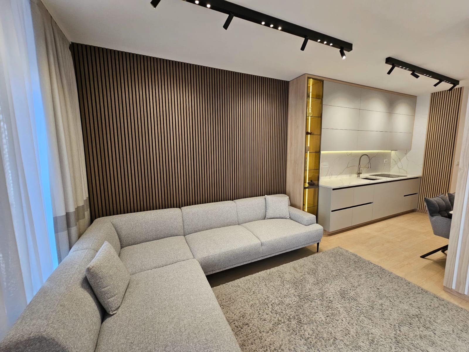 Modern living room with kitchen in an apartment in Budva, Montenegro: corner sofa, slatted wall, and stylish lighting.