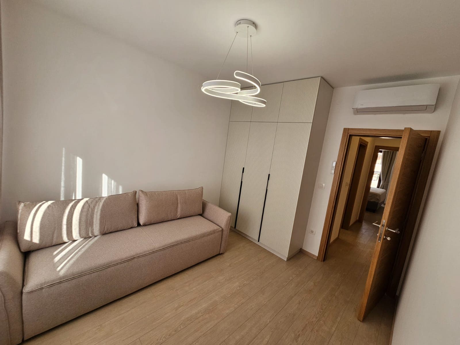 Modern living room in an apartment in Budva, Montenegro: beige sofa, built-in wardrobe, designer chandelier, and air conditioner.