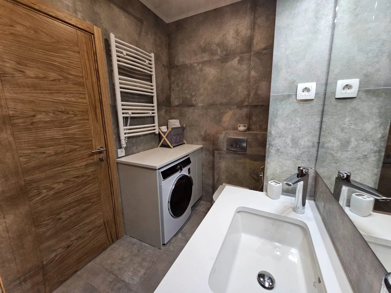 Bathroom featuring a white sink, washing machine under a counter, and a heated towel rail.