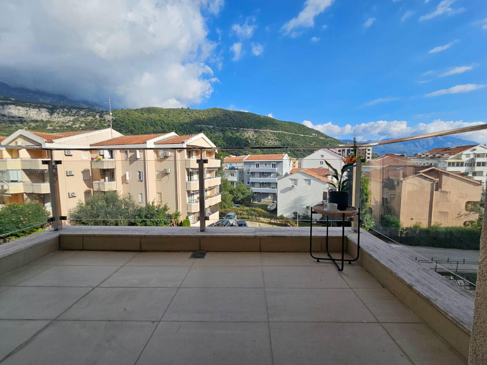 Spacious balcony with panoramic views of the mountains and city in an apartment, Budva, Montenegro, with a coffee table and railing.