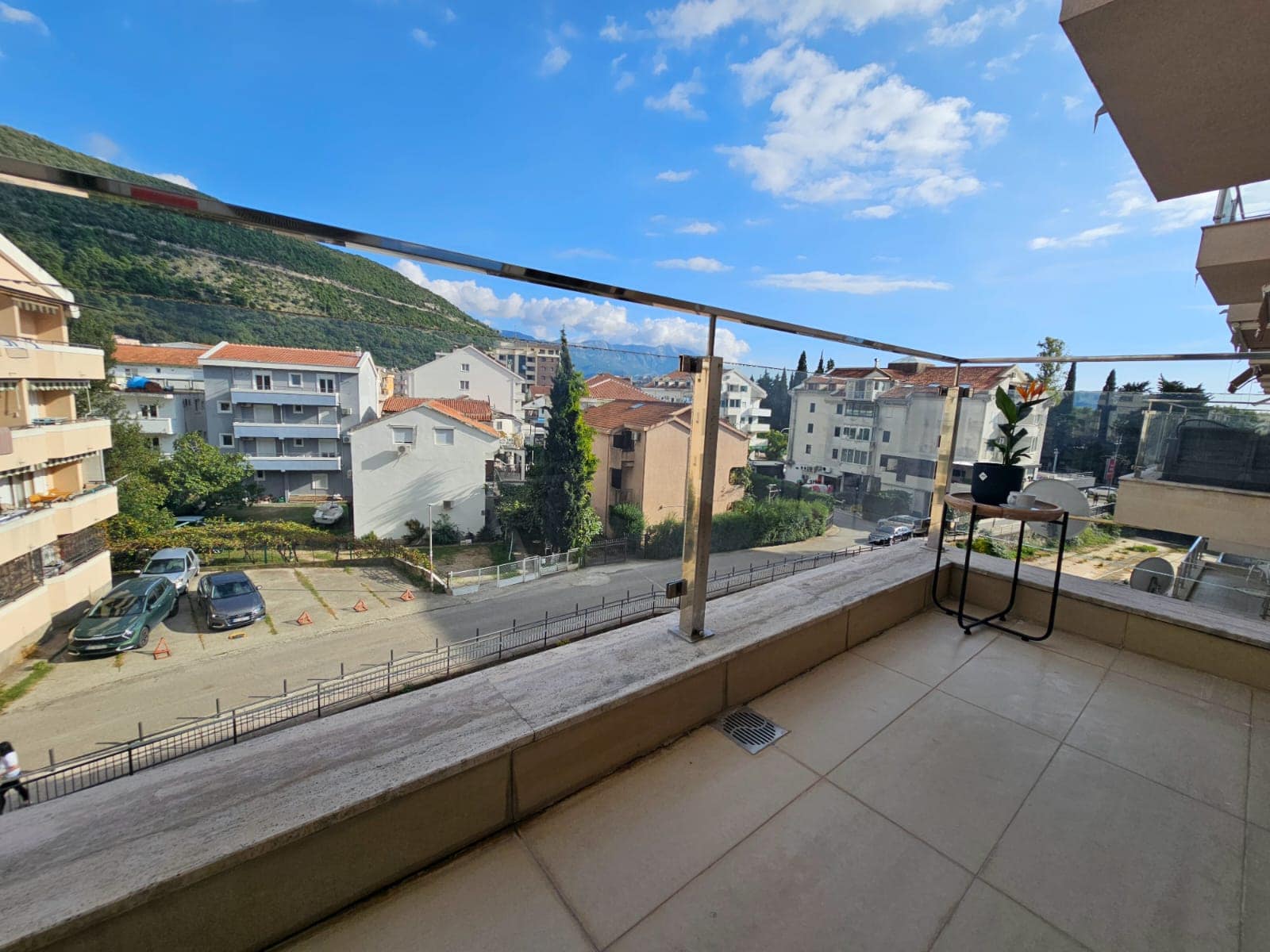 Spacious balcony with panoramic views of the mountains and the city of Budva, Montenegro, with modern glass railing finish.
