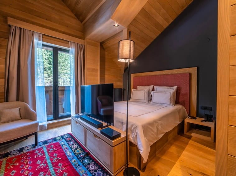 Cozy wood-style bedroom with a forest view in Kolasin residential complex, Montenegro: double bed, TV, and armchair.