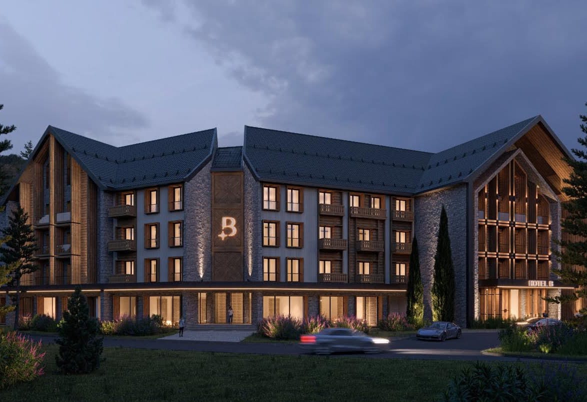 Facade of a modern chalet-style hotel in Kolašin, Montenegro: stone and wood finishes, evening building lighting.