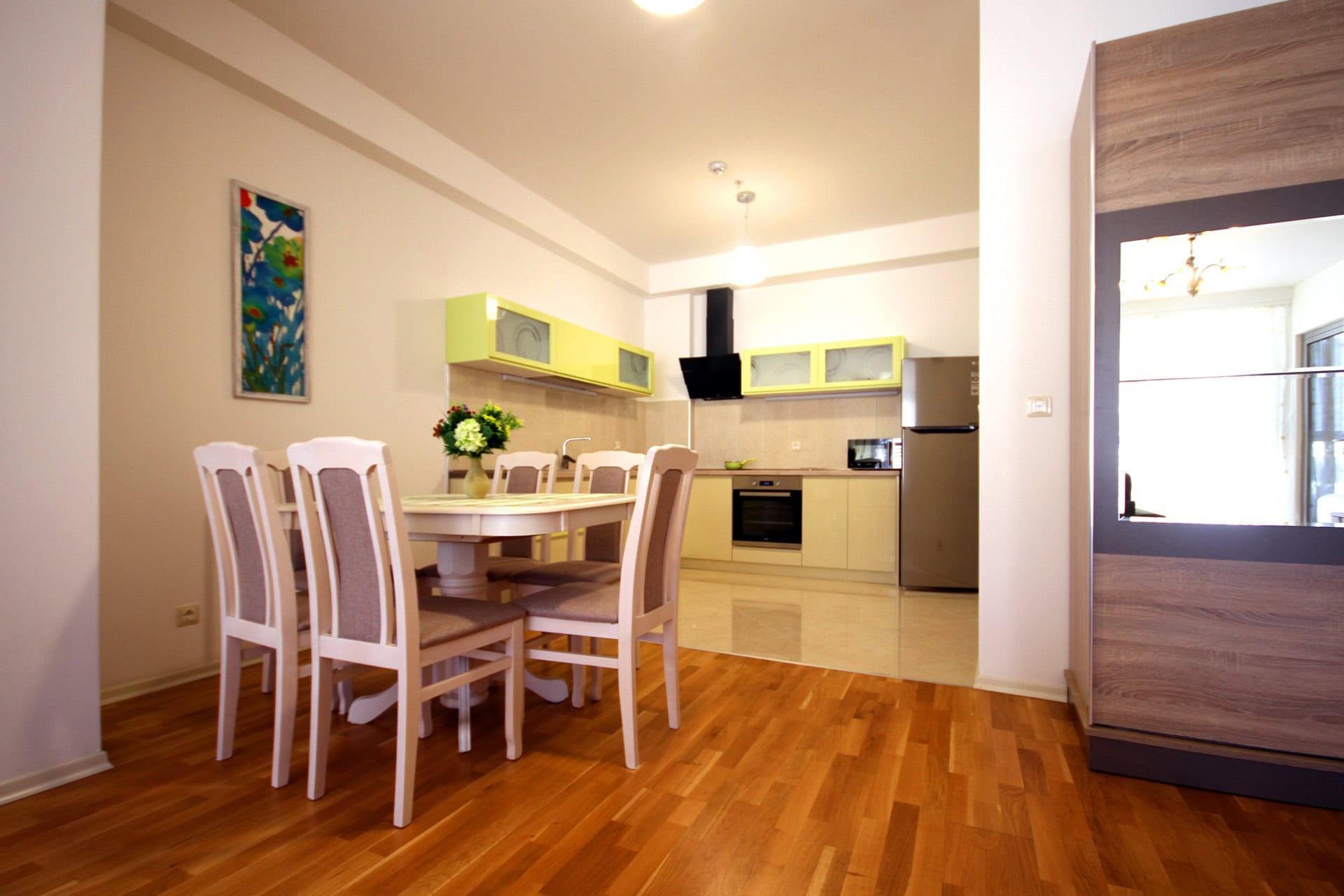 Modern kitchen-dining room in an apartment in Budva, Montenegro: light-colored cabinetry, dining area, and parquet flooring.