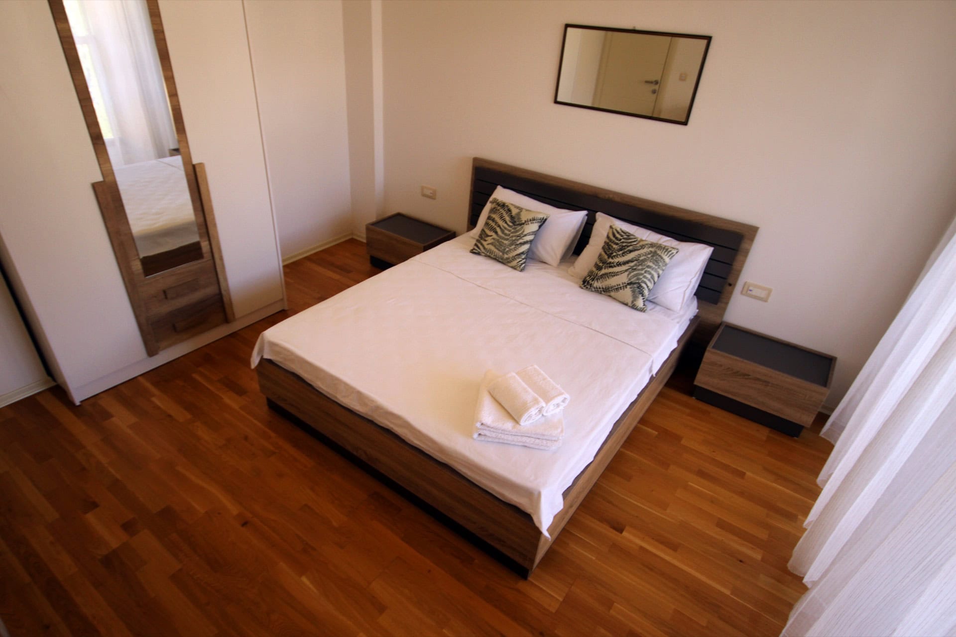 Bedroom in an apartment in Budva, Montenegro: double bed, wooden floor, mirrored wardrobe, and a bright interior.
