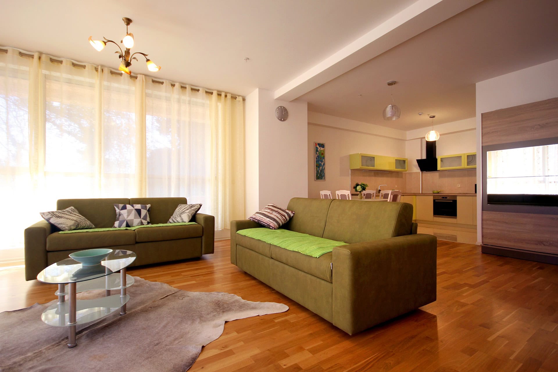 Spacious living room with kitchen in an apartment in Budva, Montenegro: two green sofas, parquet flooring, and modern furniture.
