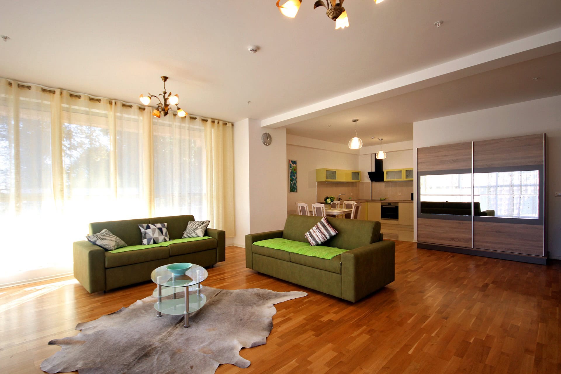 Spacious living room with green sofas and a kitchen in an apartment in Budva, Montenegro: modern interior, parquet flooring.