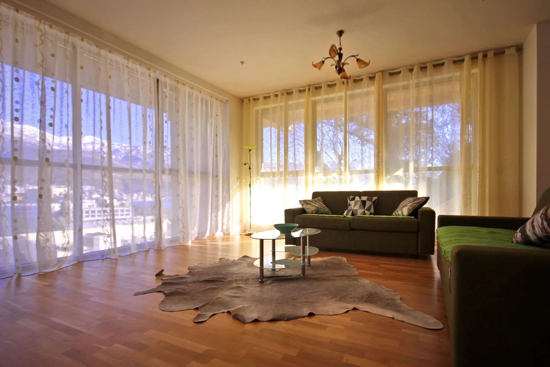 Living room with brown sofas, glass table, cowhide rug on wood floor, and large windows showing a mountain view.