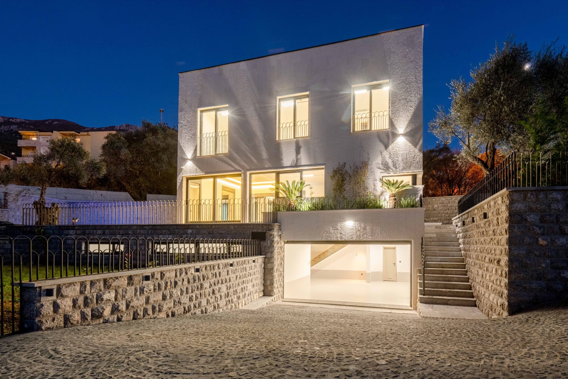 Modern villa in Kamenovo, Montenegro: illuminated facade, stone cladding, terrace, and garage in the evening.