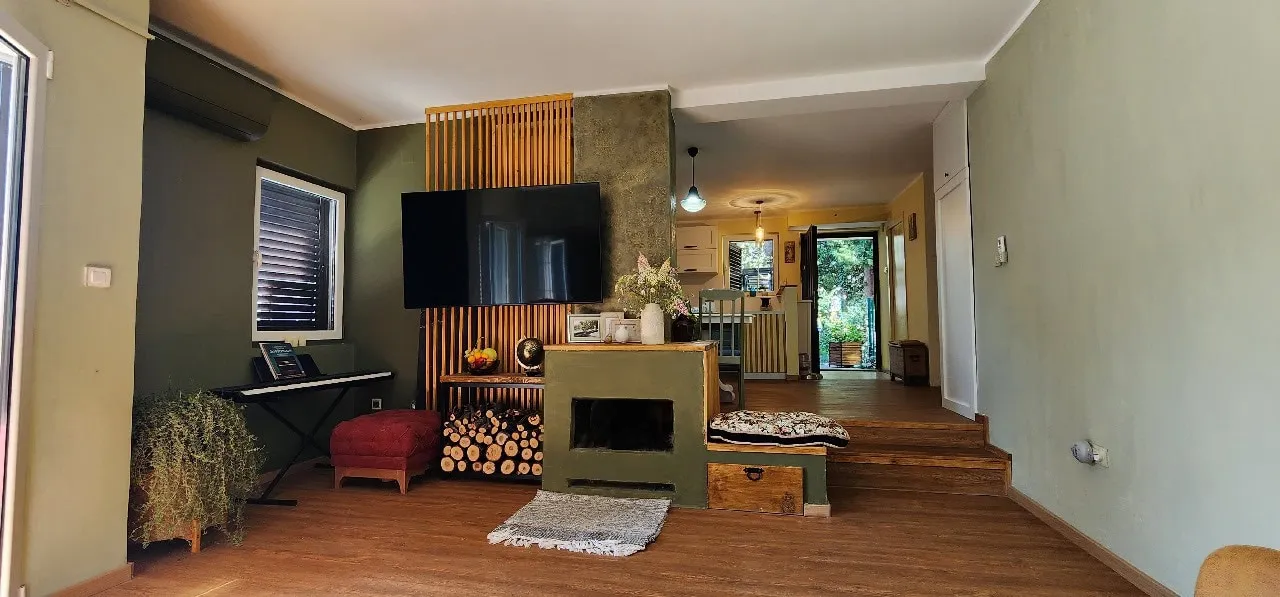 Living room with TV, fireplace, and wooden slat wall feature. Adjoining kitchen visible in background.
