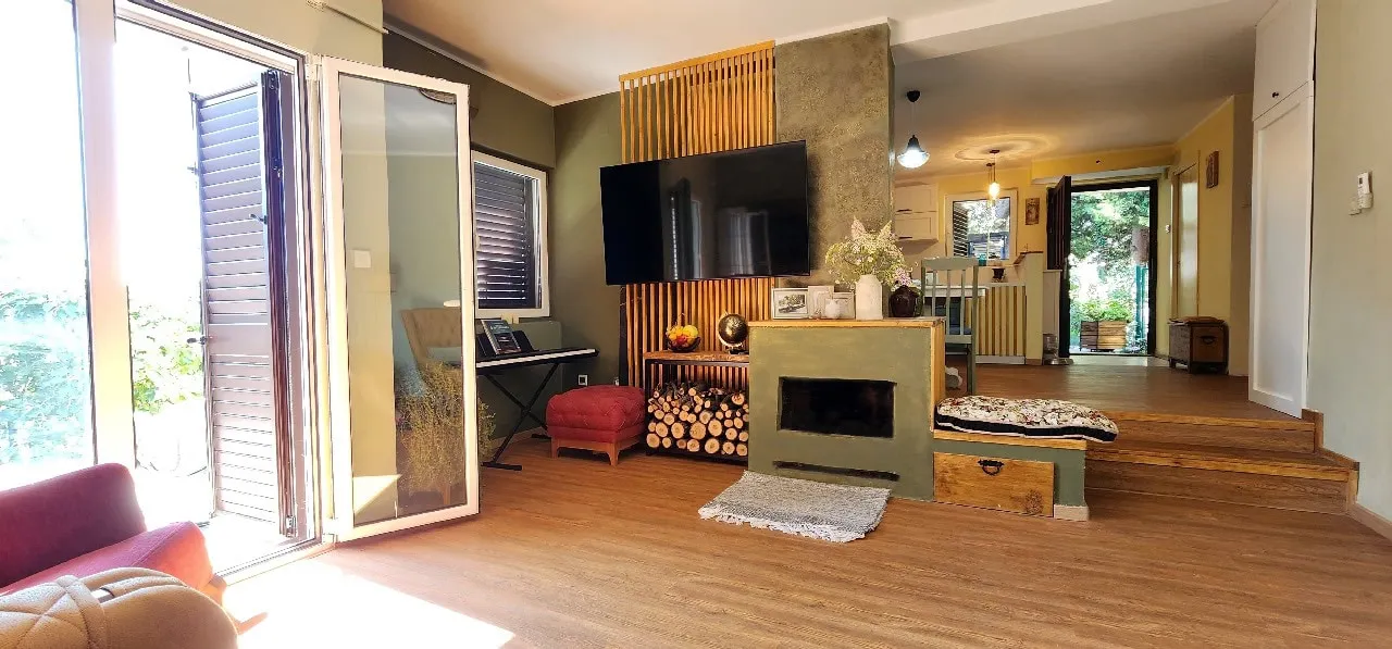 Living room featuring a fireplace, wall-mounted TV on wood slats, and large glass doors leading outside.