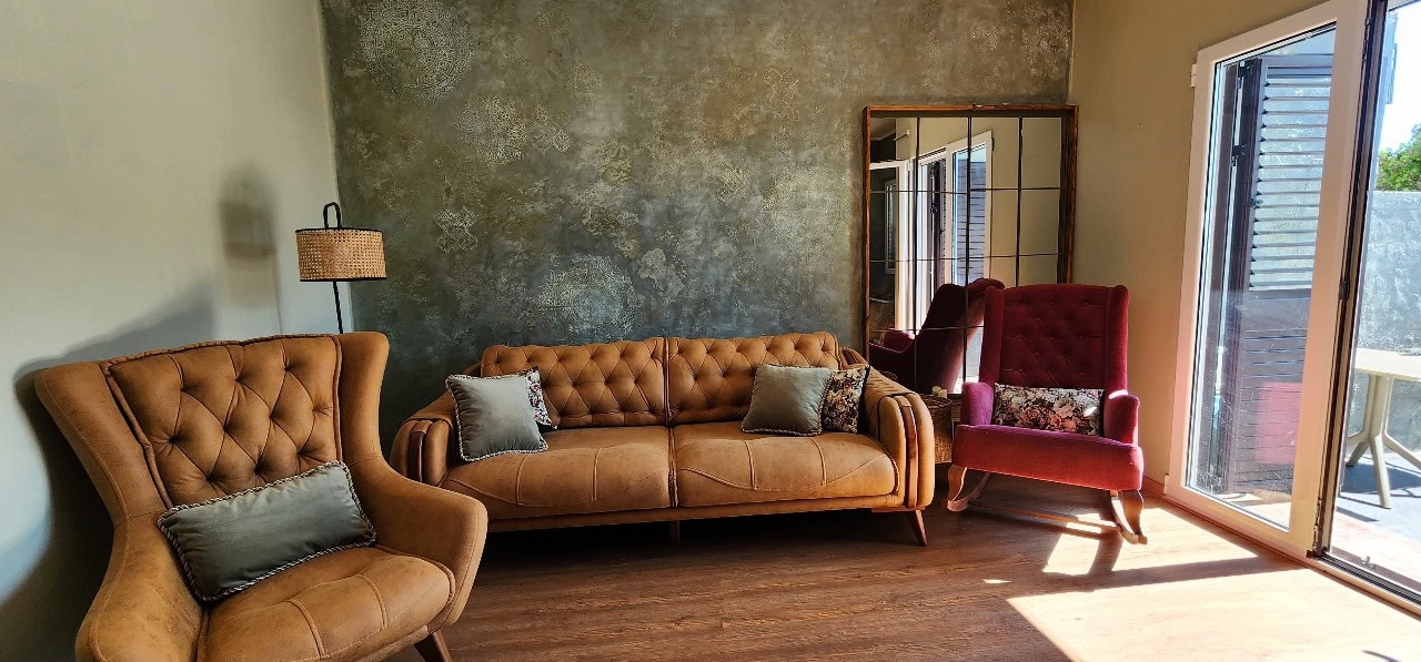 Living room featuring a brown sofa, red rocking chair, textured wall, and wooden floor.