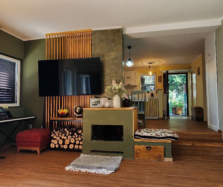 Living room featuring a TV, fireplace, and wooden slat wall. A kitchen area is visible in the background.