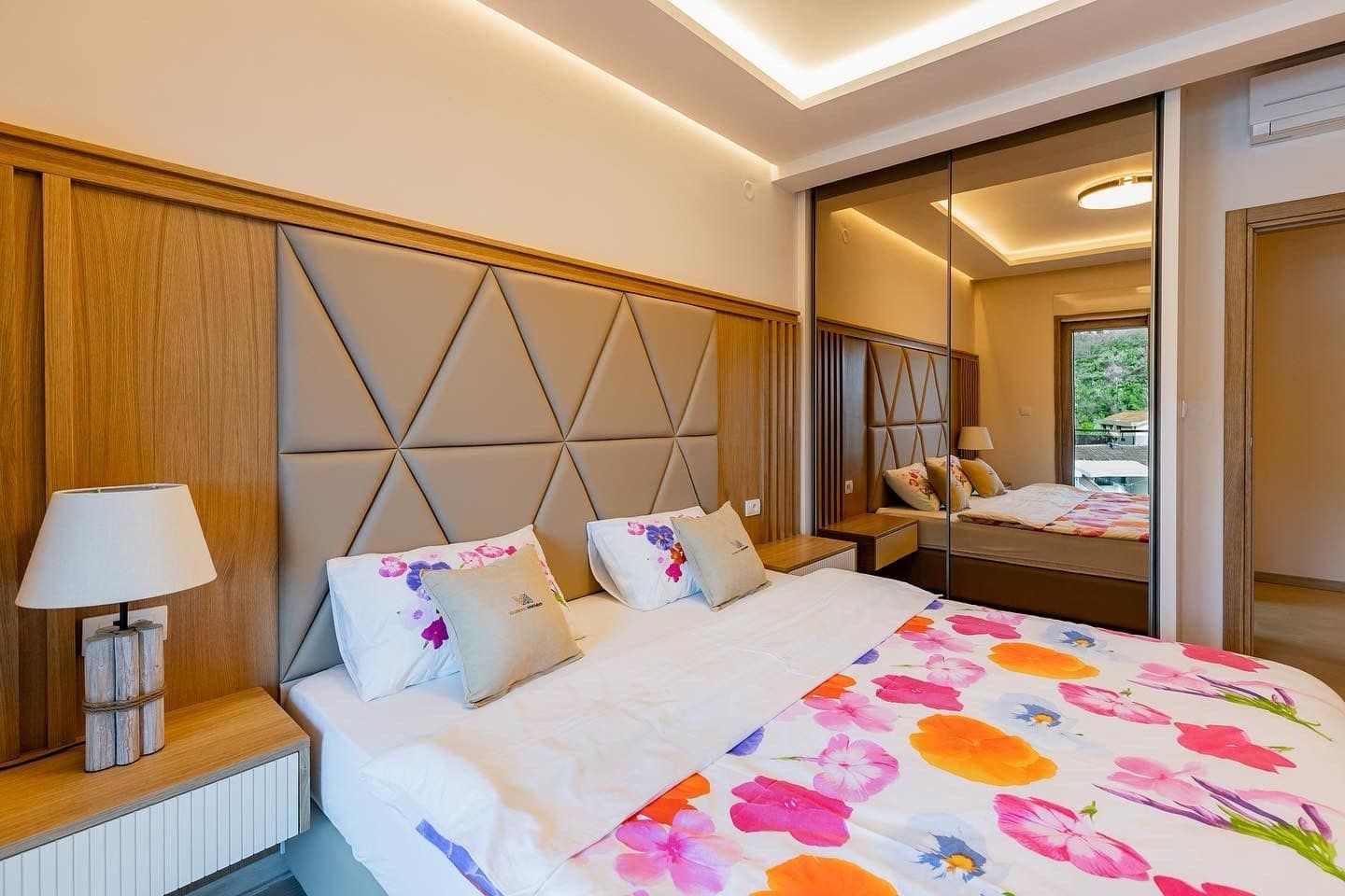 Modern bedroom in a penthouse in Pržno, Montenegro: double bed, upholstered headboard, and mirrored wardrobe.