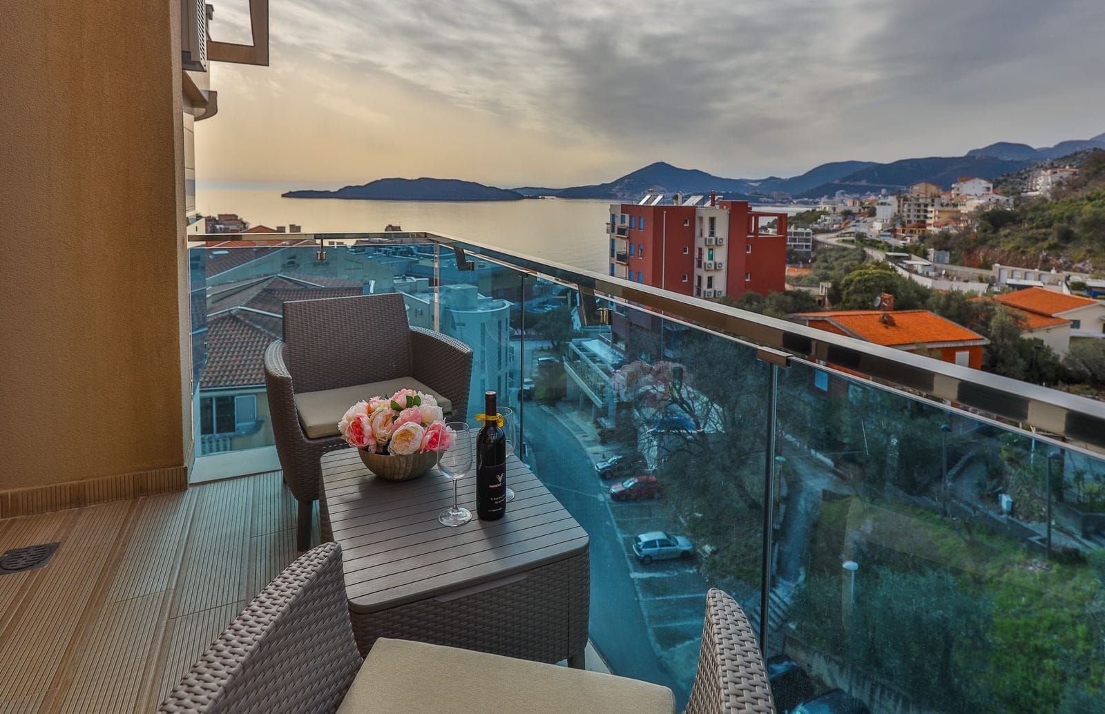 Balcony with wicker furniture and a view of the sea and city behind a glass railing.