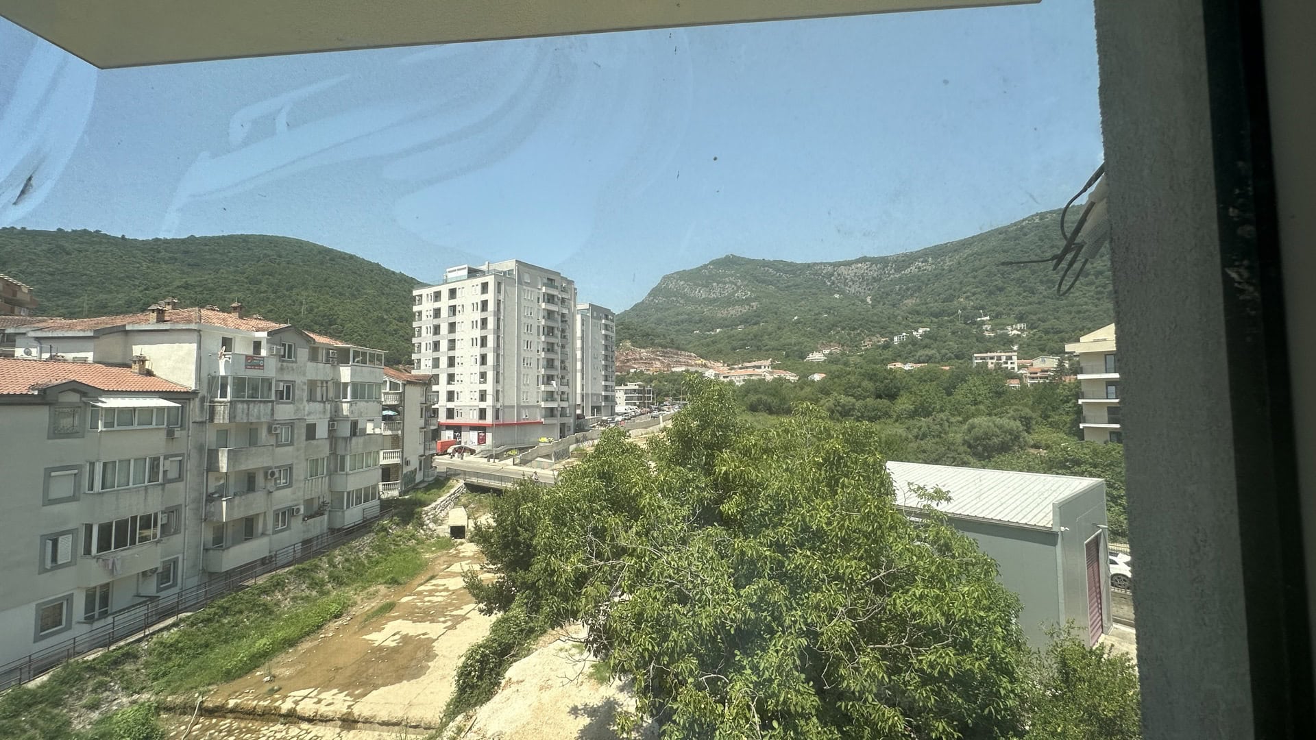 View from the apartment balcony in Budva, Montenegro: a panorama of the city, green mountains, and residential buildings on a sunny day.