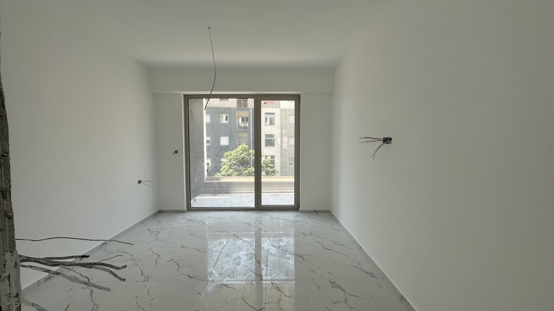 Living room in a new-build in Budva, Montenegro: light finishes, marble-look porcelain tile flooring, access to the balcony.