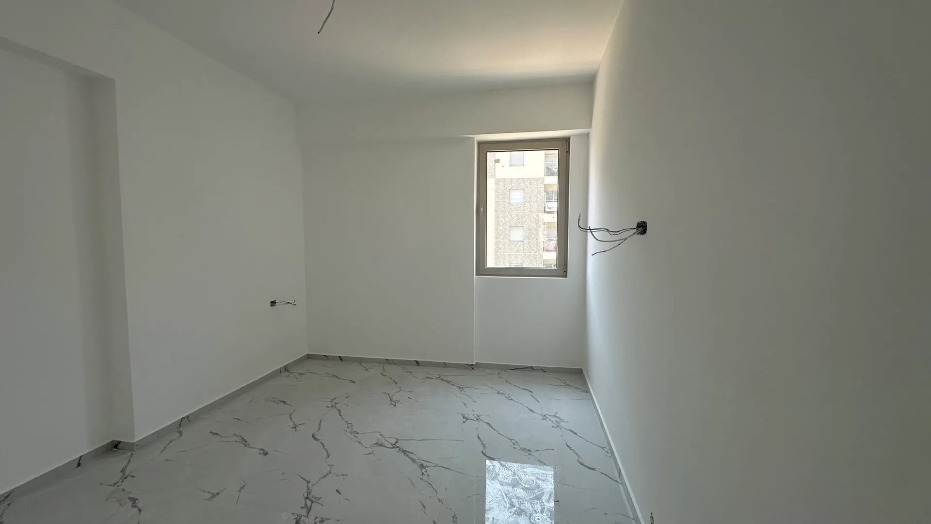 Empty room with white walls and marble floor, exposed electrical wires visible, renovation incomplete.