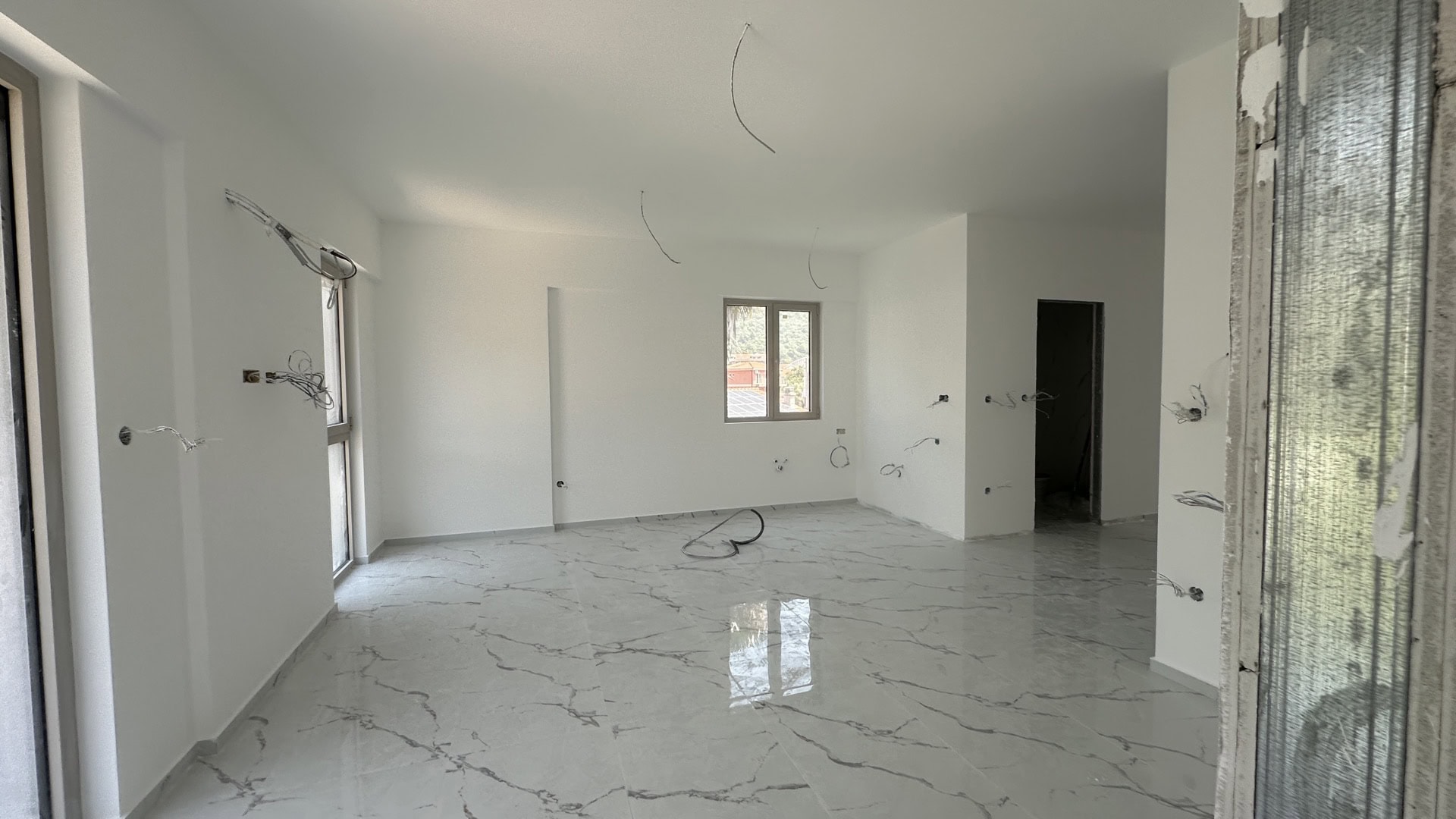 Living room in a new building in Budva, Montenegro: light finishes, marble floor, and electrical pre-installation, city view.