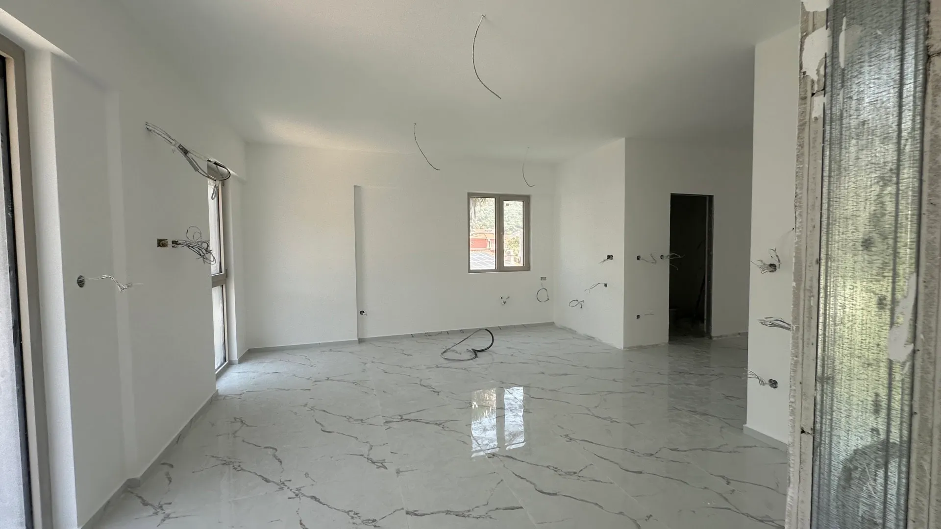 Unfurnished room under renovation with marble tiles and exposed electrical wires hanging from walls.