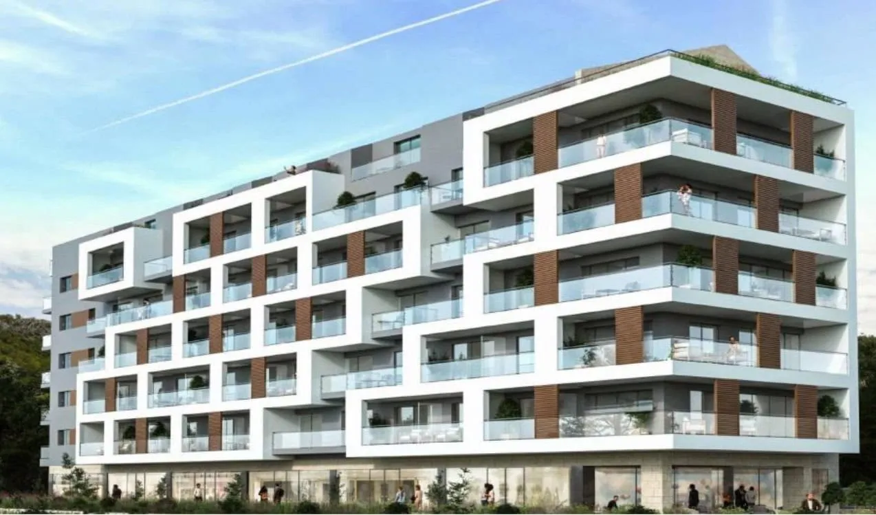Exterior view of a modern multi-story residential building featuring balconies with glass railings and large windows against a blue sky.