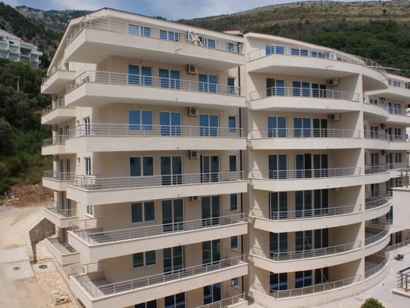Exterior view of a multi-story residential building with balconies against a hillside.