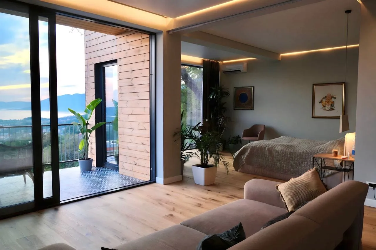 Modern bedroom featuring a sofa, bed, and sliding glass doors opening to a balcony with lake views.