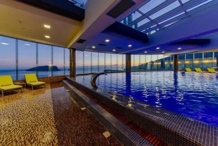 Indoor pool with panoramic sea view in a luxury residential complex in Budva, Montenegro, with a relaxation area and sun loungers.