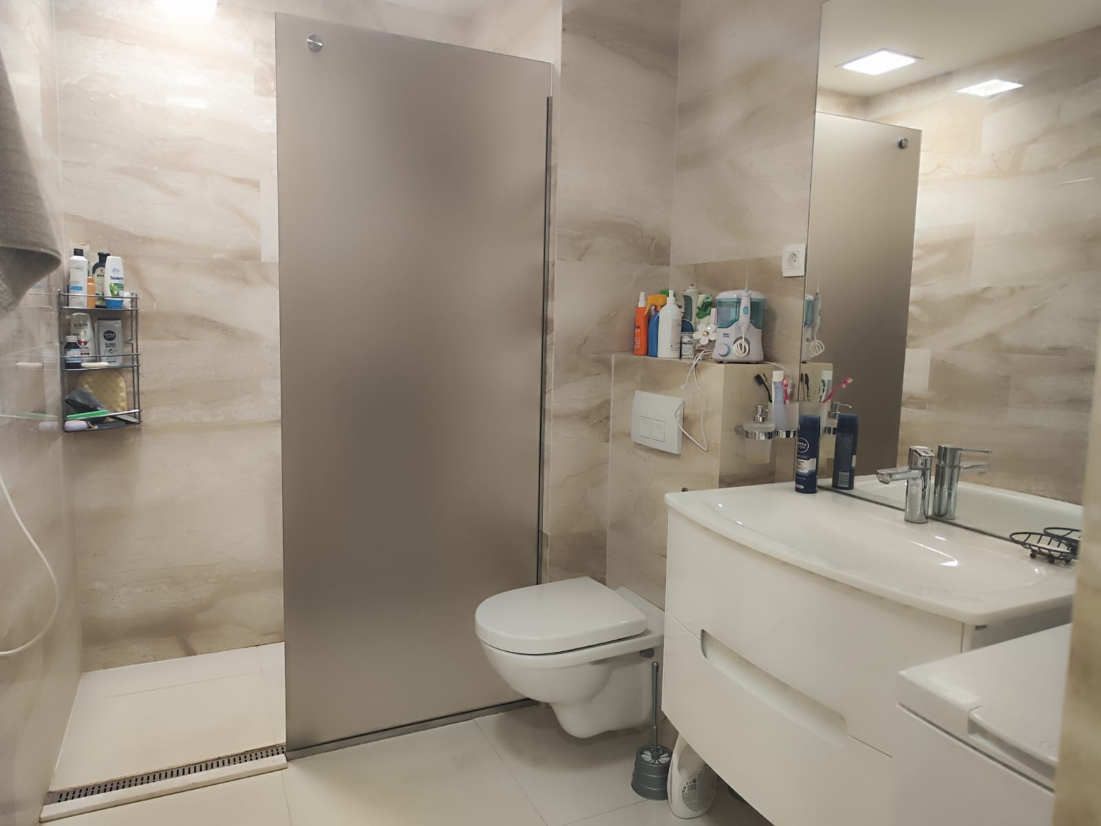 Modern bathroom in an apartment in Budva, Montenegro: shower cabin, wall-mounted toilet, and white vanity with sink.