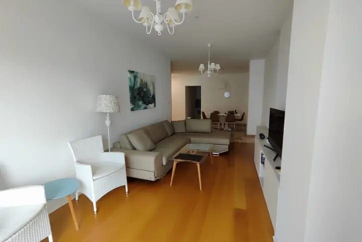 Spacious living room with a beige sofa and dining area in an apartment in Budva, Montenegro, with parquet flooring.