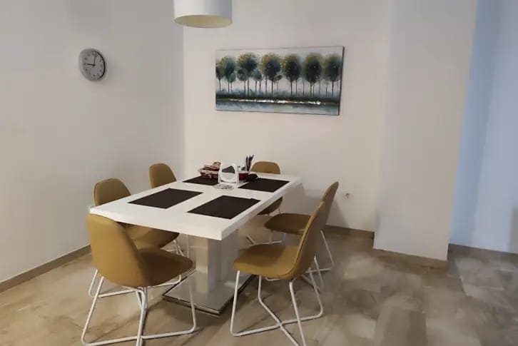 Bright dining area in an apartment in Budva, Montenegro: a white table, mustard-colored chairs, and a painting on the wall.