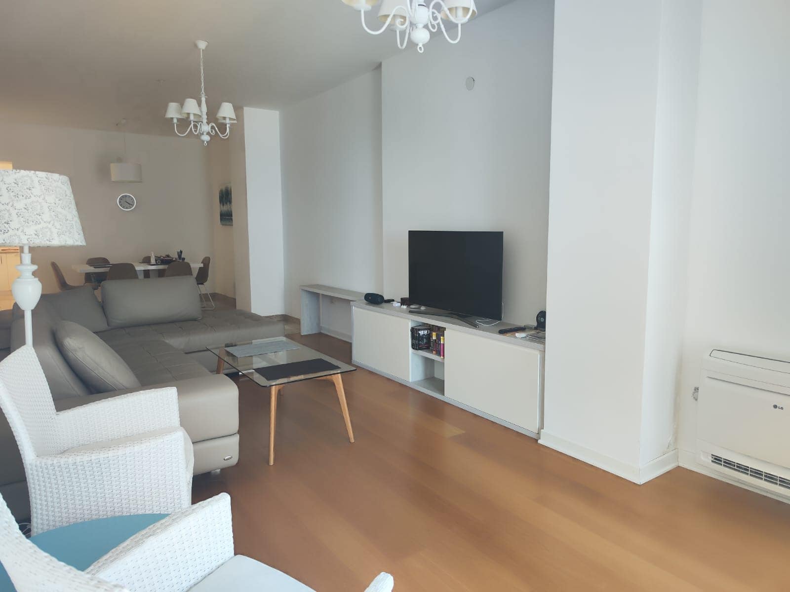 Bright living room in an apartment in Budva, Montenegro: gray corner sofa, TV area, dining set, and parquet floor.